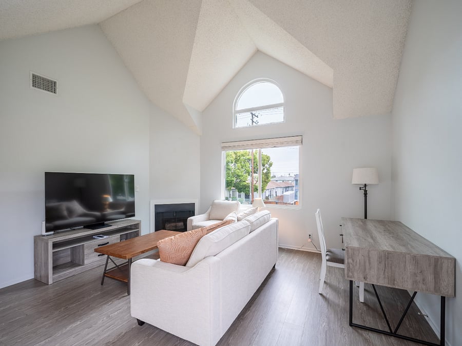 Living room with sofa, sofa pillows, chair, coffee table, end table with lamp, desk and kitchen chair, floor lamp, smart TV and console. FP.  View from front door.