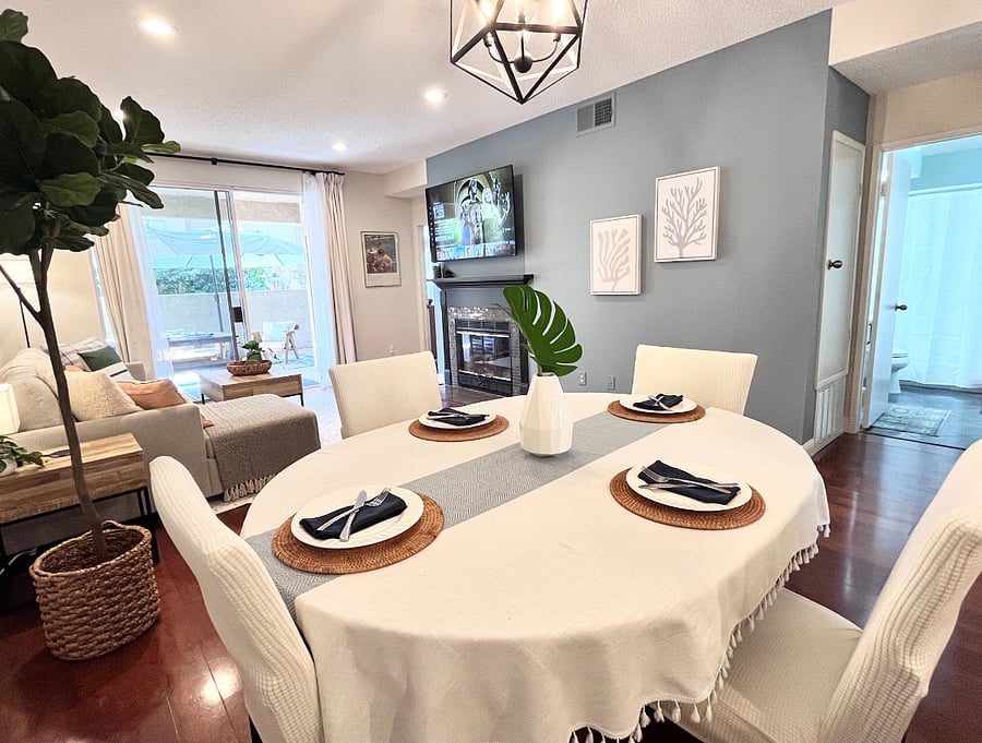 Elegant dining table for 4-6 guests with slipcovered chairs, overlooking the 65" Smart TV.