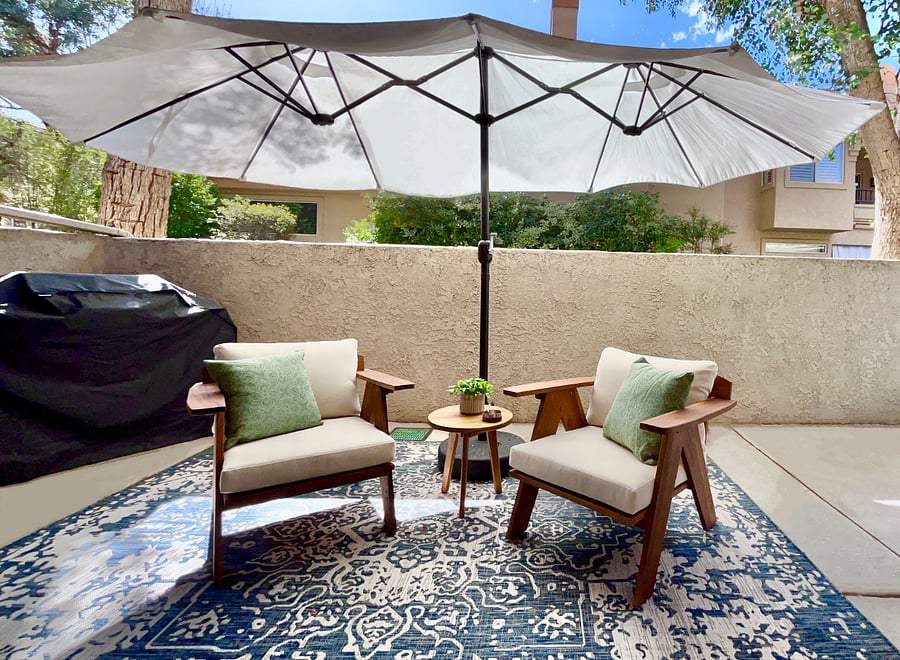 Experience the luxurious outdoor living area, featuring premium lounge chairs with a large umbrella, a propane BBQ, and serene privacy surrounded by lush treesperfect for relaxation and entertaining in style.