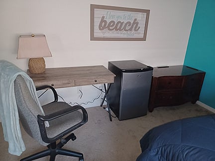 room includes desk, desk chair, throw, lamp, mini fridge and dresser shown.