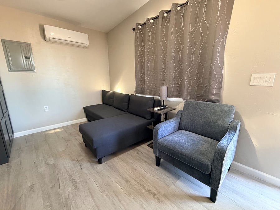 Comfortable seating area, couch, lounger and arm chair. Side rotational table with charging station, shelves, and led lamp. Bright, natural lighting.