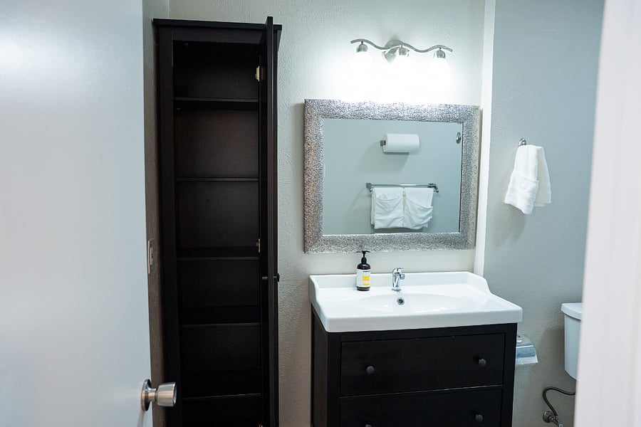 The owners bathroom is updated, clean, and spacious, stocked with essentials including shampoo, conditioner, body wash, fresh towels, paper towels, and toilet paper. Additionally, it has a cabinet with shelves and the door has a full length mirror.