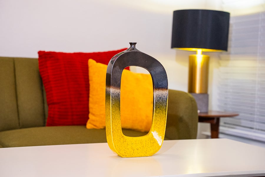 The artwork throughout the space features bold, colorful pieces that echo a midcentury modern aesthetic. Abstract floral canvases, graphic prints, and sculptural objects bring in rich reds, yellows, blues, and greens that play off the furniture and decor. Each piece has clean lines and simple shapes, adding personality and warmth without feeling cluttered. Together, they create a cohesive, vibrant gallery feel that ties the living and dining areas into one stylish, welcoming home.