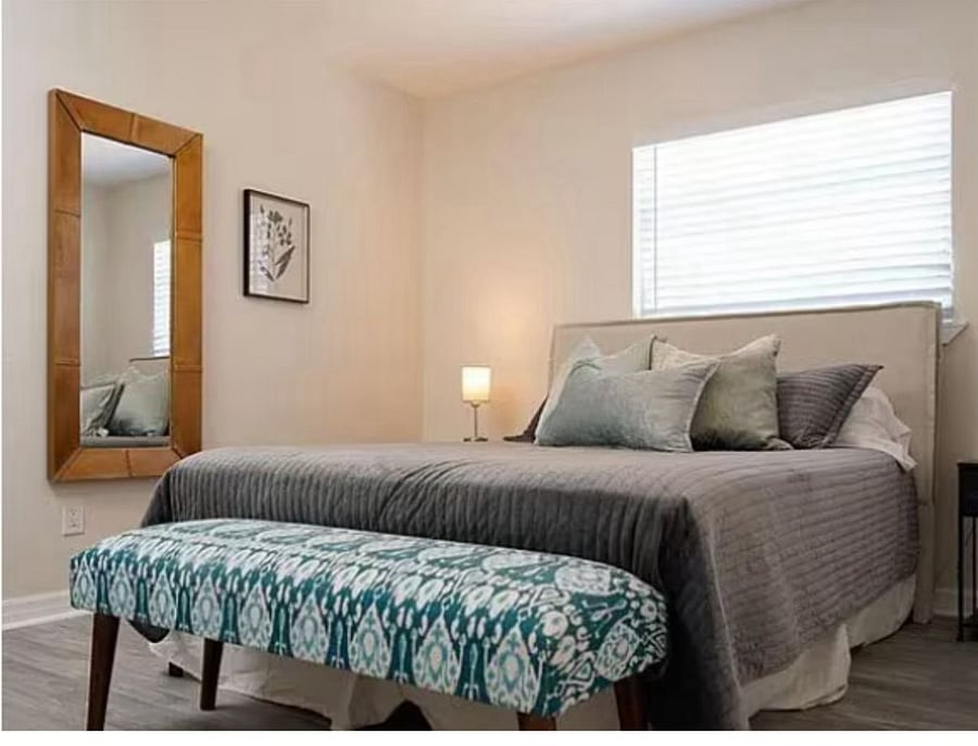 Stylishly furnished private bedroom with queen bed, full-length mirror, nightstands, and warm lighting