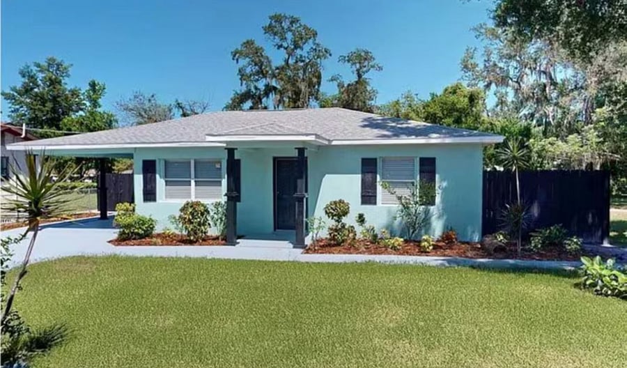 Well-maintained exterior with lush lawn, mature trees, privacy fence, and covered carport