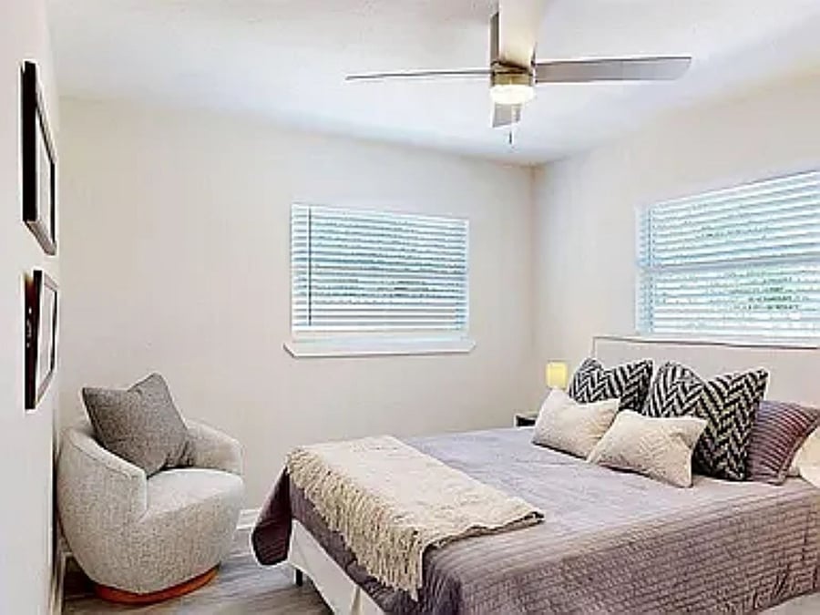 Fully furnished, cozy bedroom with a plush bed, lounge chair, natural light, and climate-controlled comfort, move-in ready.