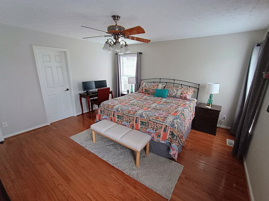 The primary bedroom features a workstation with a desk, chair, keyboard, and two monitors, along with a king size bed and a bench for added comfort.