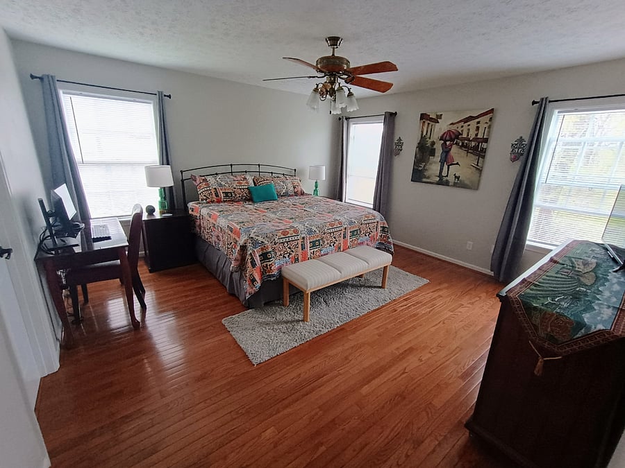 The primary bedroom features a workstation with a desk, chair, keyboard, and two monitors, along with a king size bed and a bench for added comfort.