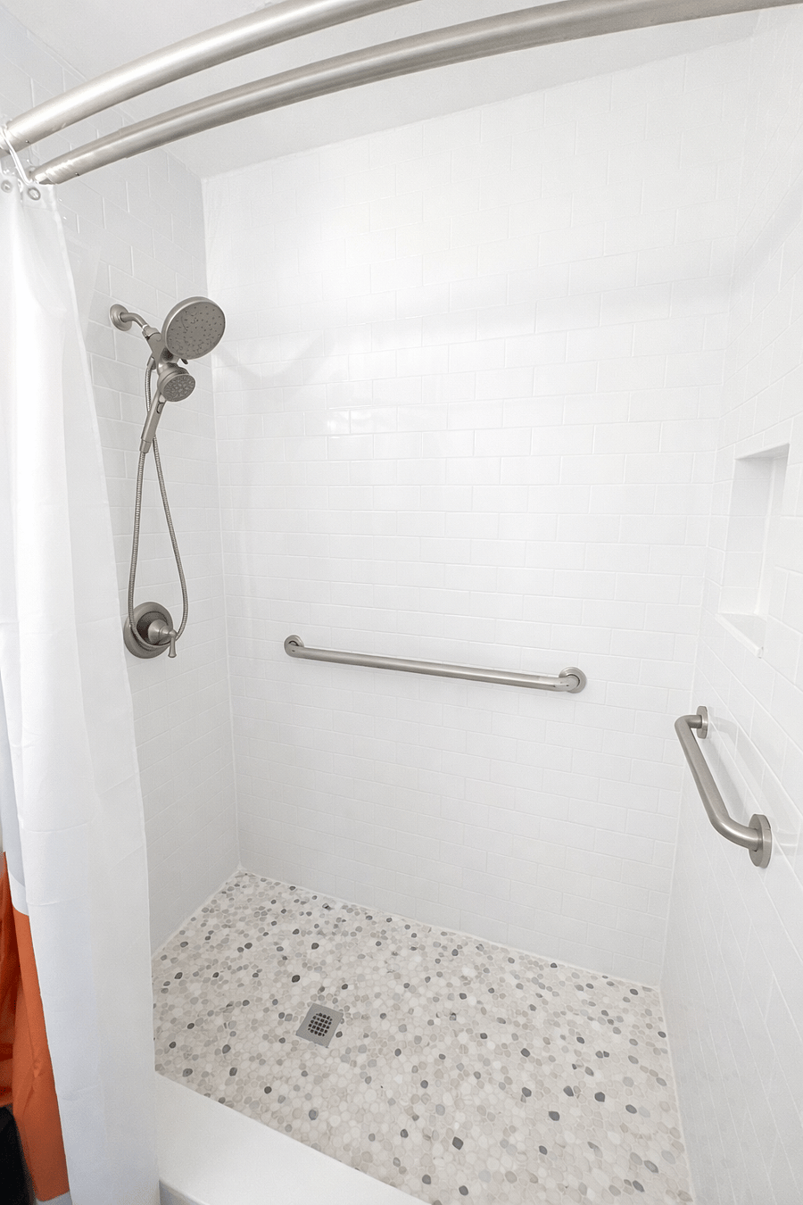 Spacious walk-in master shower featuring grab bars for added support, a handheld shower head, and a clean, bright design for comfort and ease of use.