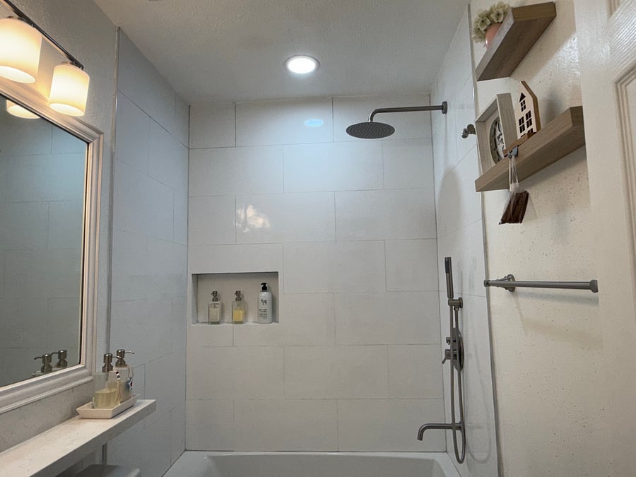 Full view of the newly remodeled bathroom showing the full-size tub, rain shower, handheld shower, built-in niche, vanity area, and updated lighting.