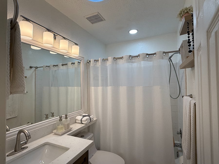 Bright and clean bathroom with tub, natural light, fresh towels, shampoo, hand soap, toilet paper, and bath essentials.