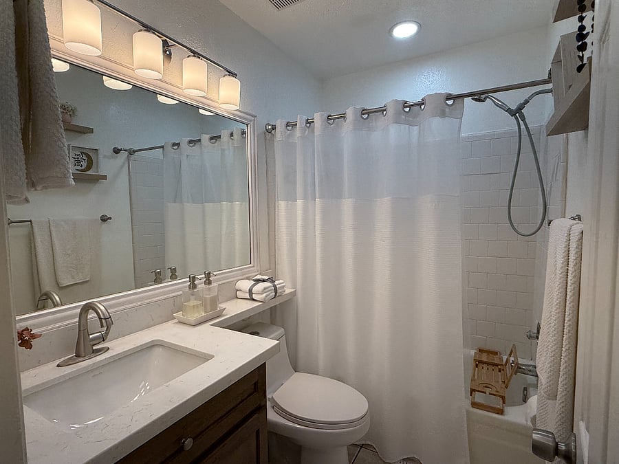 Dedicated bathroom with natural light, warm wood vanity cabinetry, large mirror, updated lighting, and a modern pull-down faucet.