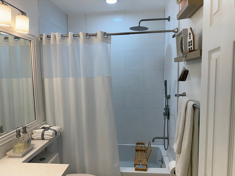 Newly remodeled dedicated bathroom for the resident's exclusive use, featuring a full-size tub, stainless-steel rain and handheld showers, built-in niche, and contemporary tile