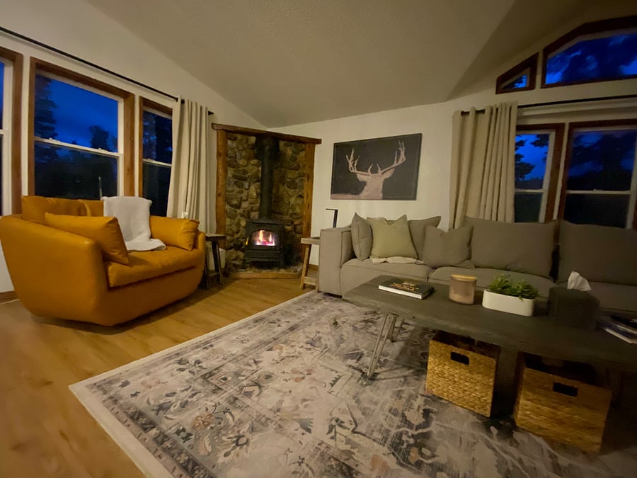 Very cozy living room with leather swivel chair, oversized sofa and large ottoman, gas fireplace, and opposite wall is covered by a large flat screen TV with sound bar.