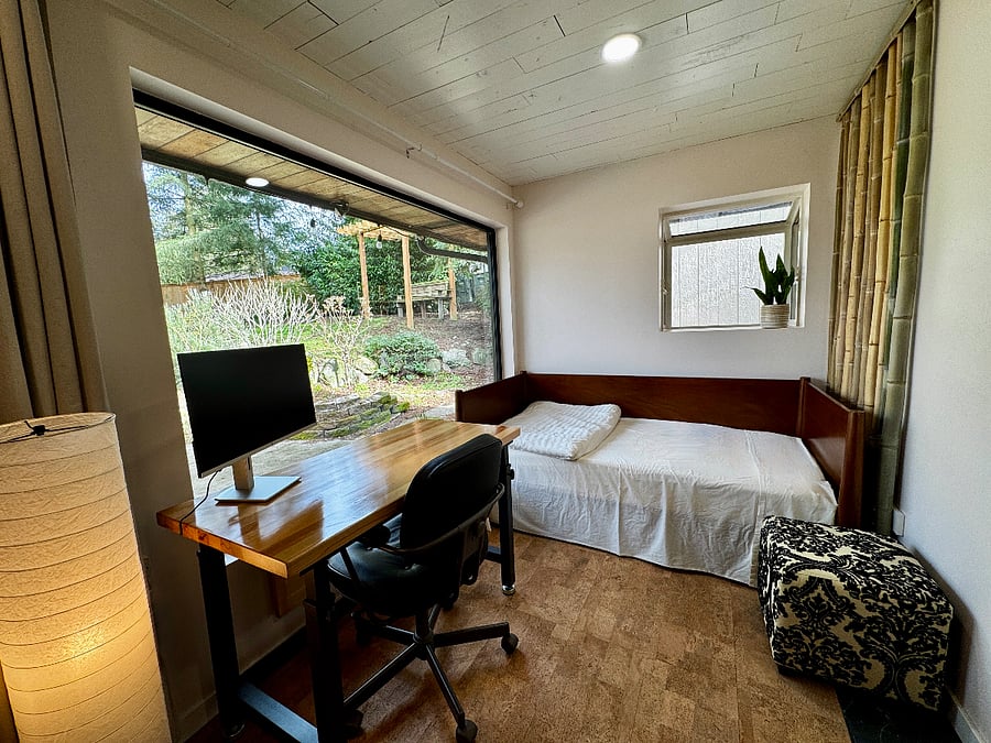 This is a workspace with a twin daybed. There is an adjustable height desk and ergonomic chair with monitor, a box fan with merv 13 filter, and an armoire with bed and bathroom linens. The large window opens to the private fenced backyard.
