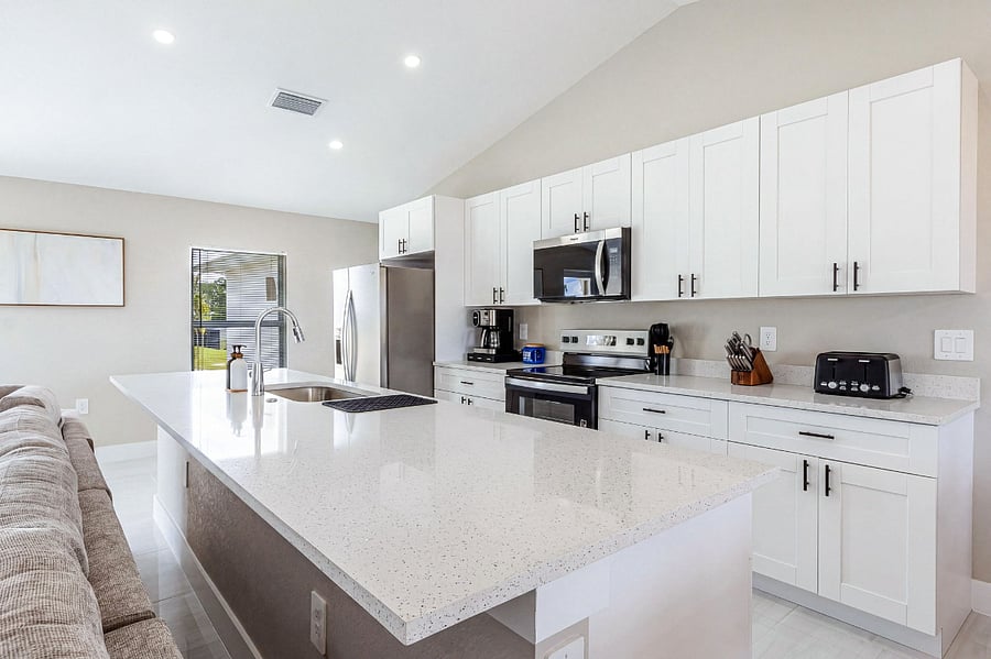 Kitchen galley view showing the full-length quartz island, stainless dishwasher, and a bright open sight line through to the living area and backyard a cook's dream with natural light throughout.