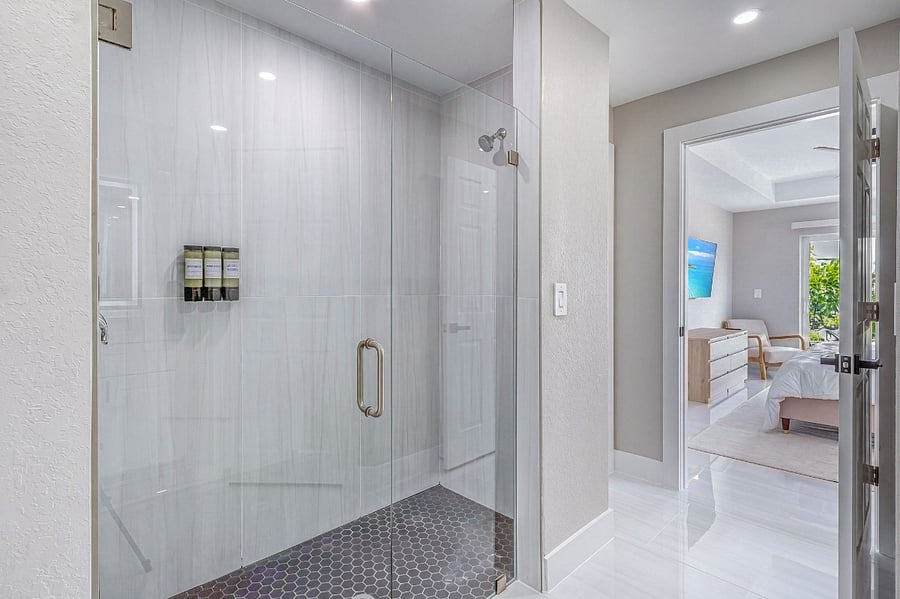 Primary en-suite bathroom featuring a large walk-in glass shower with floor-to-ceiling tile, hex mosaic floor tiles, and brushed gold hardware a luxurious spa-like experience.