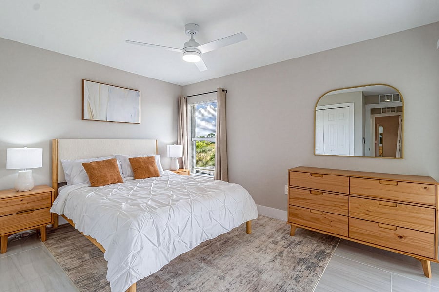 Second bedroom with a queen-size bed, sliding glass door access to the patio, ceiling fan, and warm neutral dcor with rattan wall accents. Light, airy, and comfortable.
