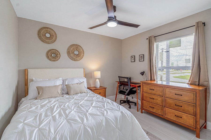 Versatile fourth bedroom with a full-size bed, built-in desk and ergonomic chair, large wood dresser, and rattan wall art perfect for traveling professionals or longer-term stays.
