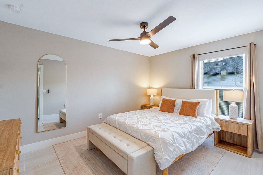 Third bedroom with a queen-size bed, ceiling fan, natural wood dresser, gold-framed arched mirror, and warm neutral tones. Cozy and well-appointed for a restful night's sleep.