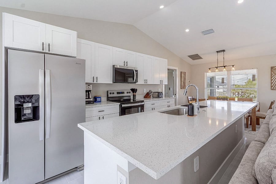 Expansive kitchen island with quartz countertops offers plenty of prep space and seating. White shaker cabinets line the walls, complemented by a full suite of stainless steel appliances and modern matte black hardware.