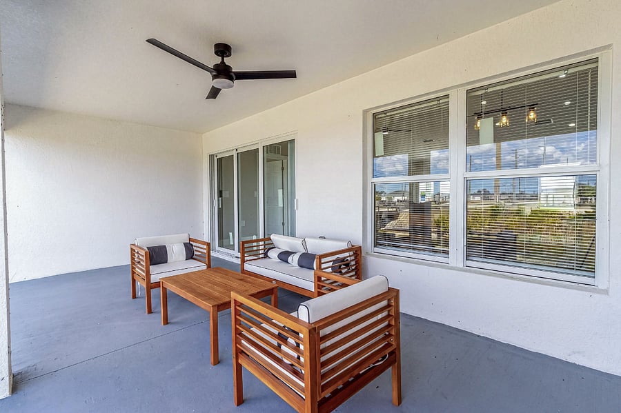 Spacious covered lanai with teak lounge seating, ceiling fan, and wide sliding glass doors opening to the living room seamless indoor-outdoor flow for a true Florida lifestyle.