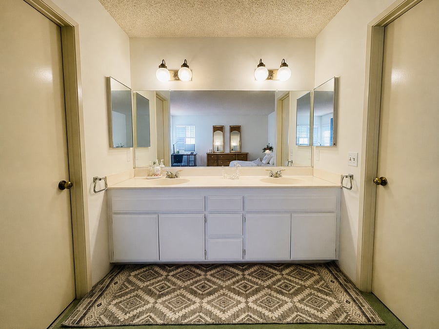 Large vanity with dual sinks and excellent lighting. Bathroom on the left, closet equipped with mini fridge and microwave on the right.