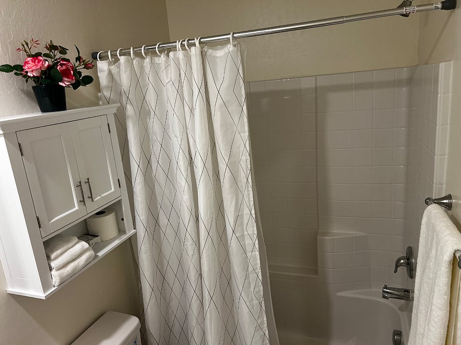 Full Bathroom 1 - Toilet Bowl with Bidet/Water Sprayer, Bath Tub/Shower with Curtains, Cabinets with towels, and sink.