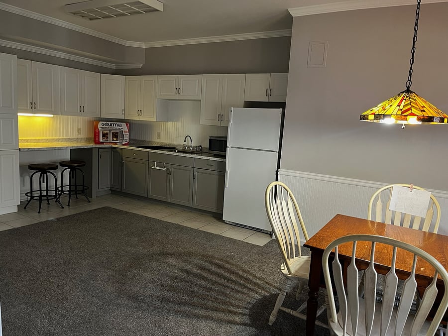 Kitchenette (will be fully furnished) with sink, stovetop, air fryer/oven, microwave, full-size fridge, kitchenware, and two bar stools.