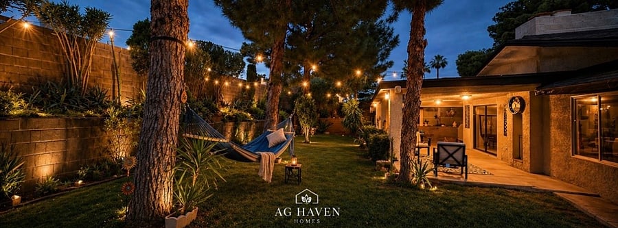 Private backyard retreat with covered patio, BBQ grill, outdoor cooking stove, lounge seating, hammock, and ambient evening lighting.