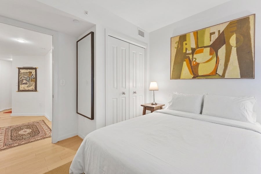 A bright, minimalist retreat offering ample closet space, a full-length mirror, and cozy bedside lighting.
