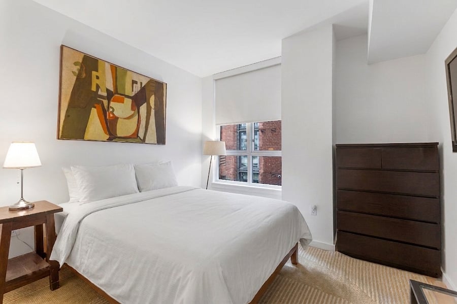 Wake up to natural light in this serene bedroom featuring a plush queen bed and large windows with privacy shades.
