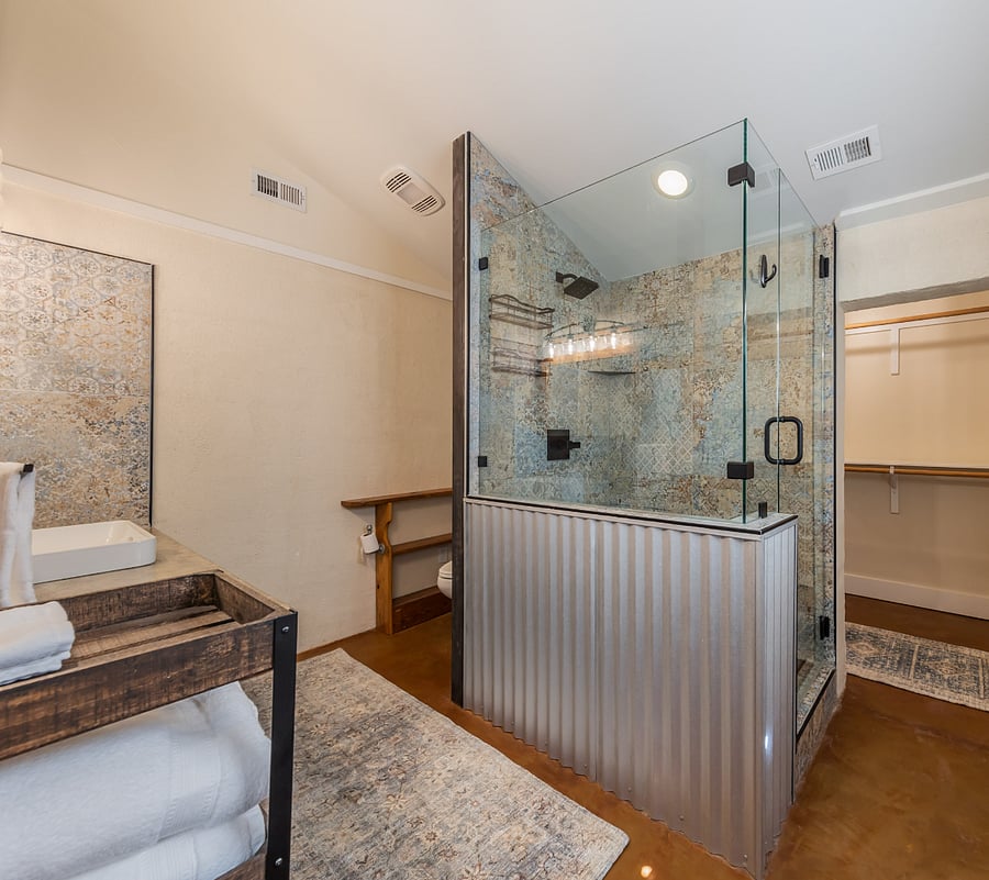 Tiled shower with glass enclosure and a corrugated metal half-wall.