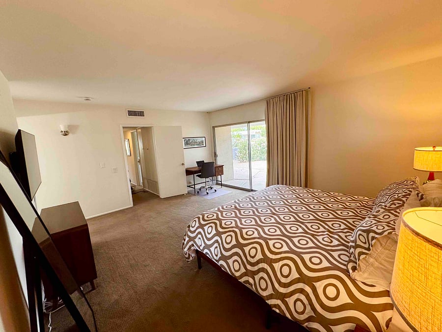 Primary bedroom with full-length mirror, drawers, desk and patio views
