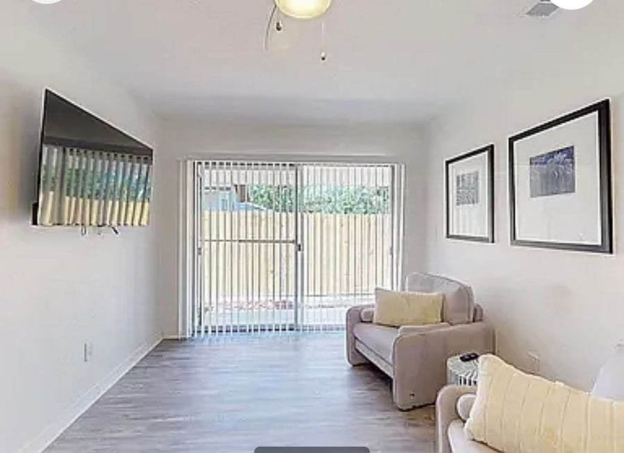 Comfortable shared living space with wall-mounted TV, ceiling fan, and sliding door to the fenced backyard