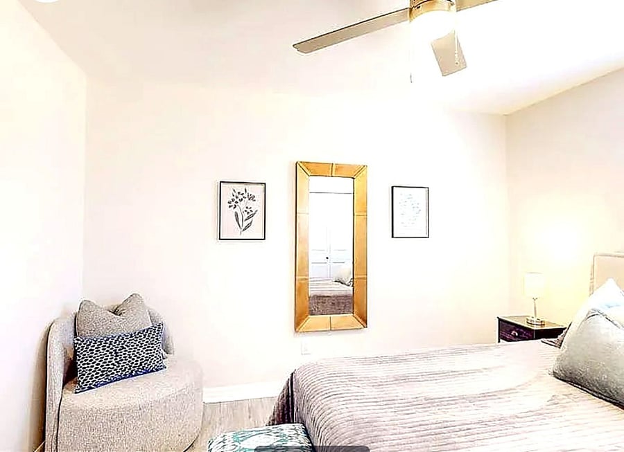 Stylishly furnished private bedroom with queen bed, full-length mirror, nightstands, and warm lighting