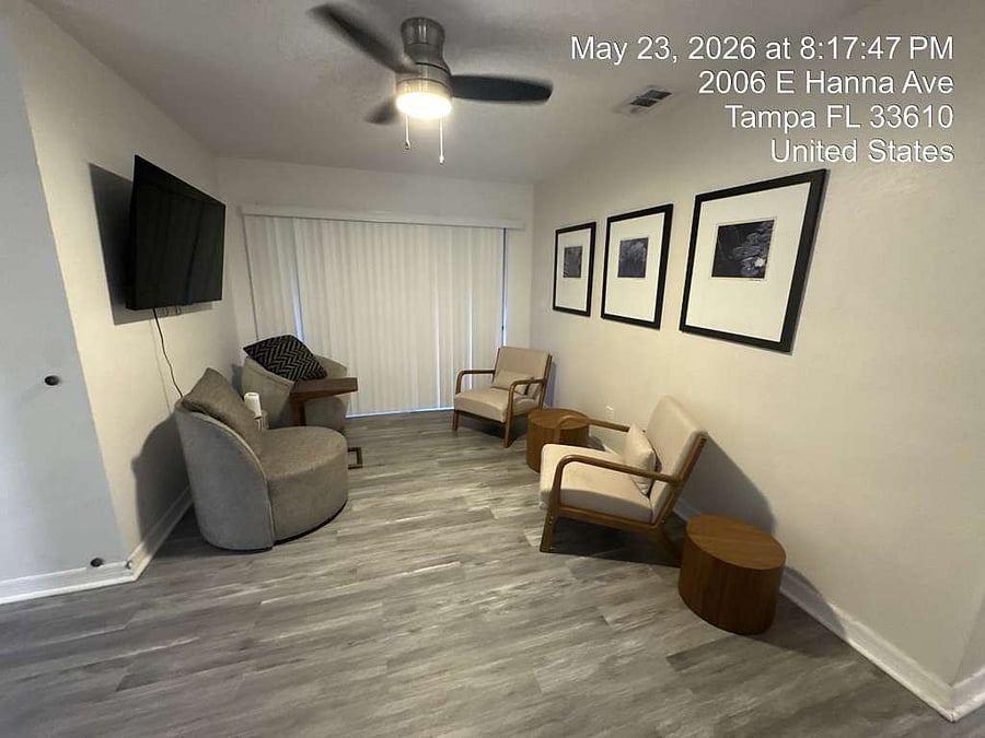 Comfortable shared living space with wall-mounted TV, ceiling fan, and sliding door to the fenced backyard