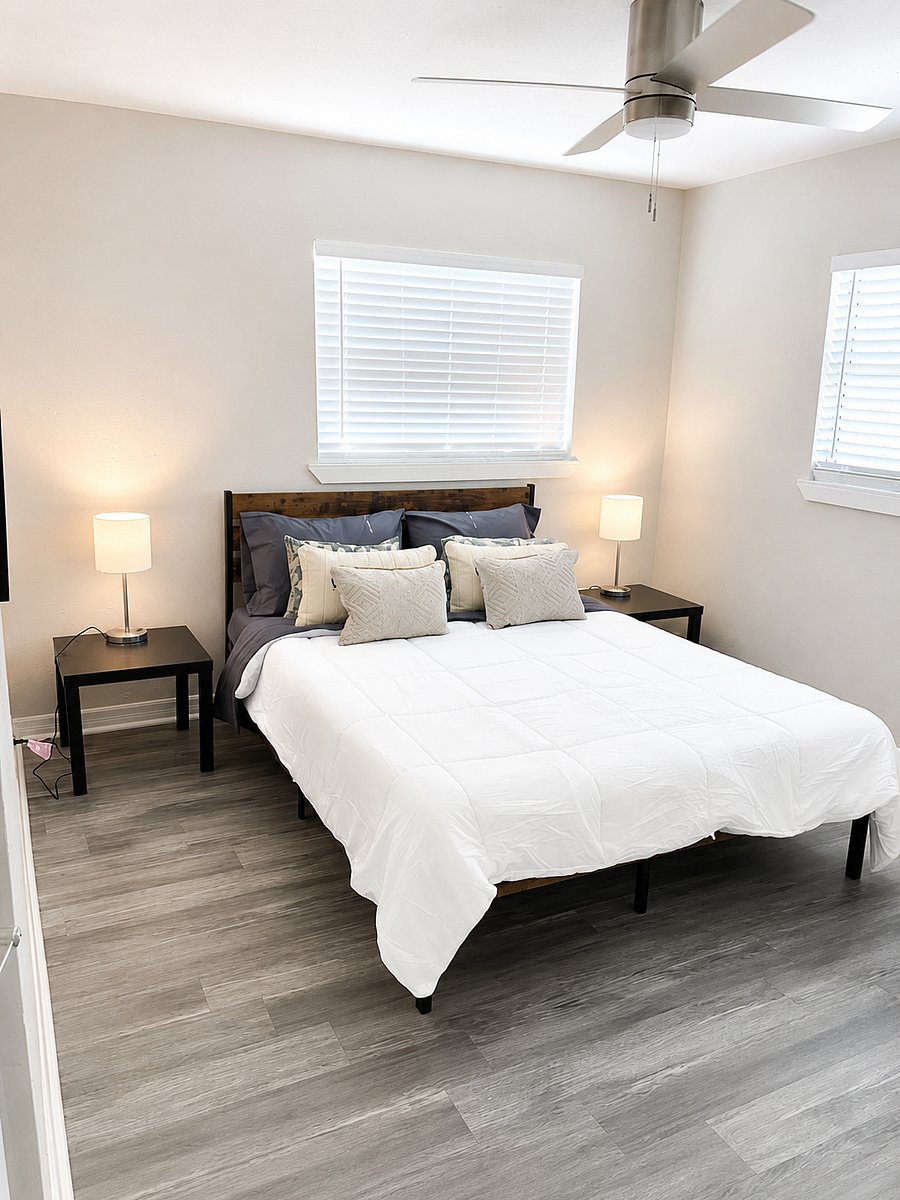 Modern bedroom featuring large windows, ceiling fan, and minimalist dcor.