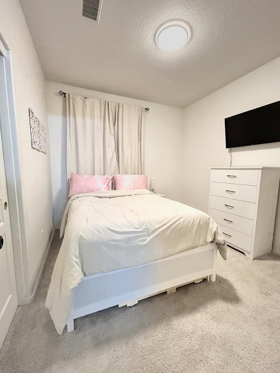 3rd bedroom with tall dresser, mounted Smart TV, closet, and blackout curtains.
