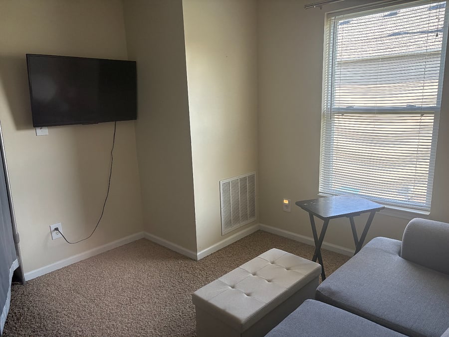 Loft-area living space includes love seat, Roku tv, end table with lamp, tv tray, and storage ottoman.