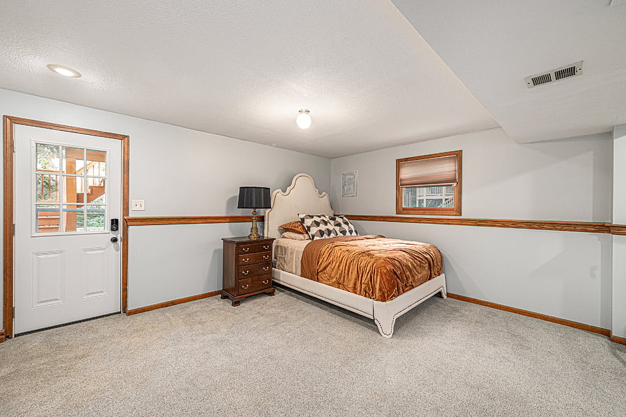 Enjoy a large, airy basement bedroom with simple yet elegant design, complete with a table, cabinet, and bedside lamp for comfort and style.
