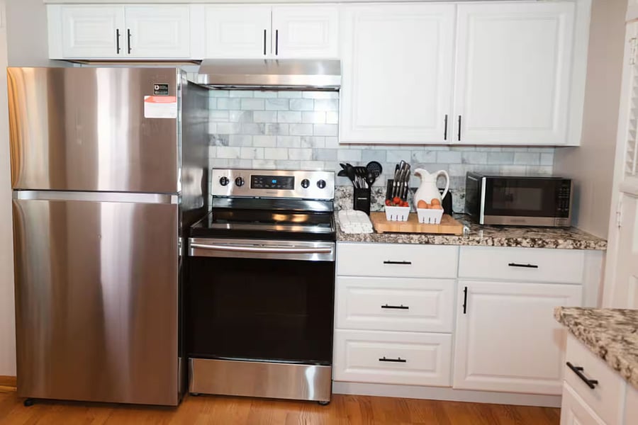 Kitchen with a stove, oven, refrigerator, freezer, dishwasher, toaster, blender, and hot water kettle, cooking basics, baking sheets, dishes, silverware, wine glasses, and a coffee maker with coffee.