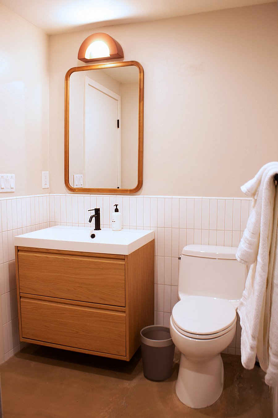 Charming secondary bathroom showcasing a warm wood floating vanity, vertical stack wainscoting tile, and a statement arch light accent.