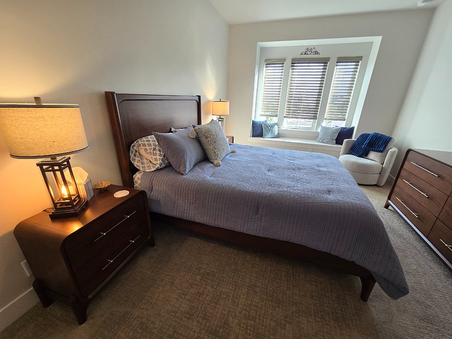 Bedroom 2 is a spacious and inviting room, furnished with new furnishings including a queen-sized bed, a dresser, two nightstands, a full-length mirror, a cozy chair, and a seated window bench, creating a comfortable and stylish retreat.