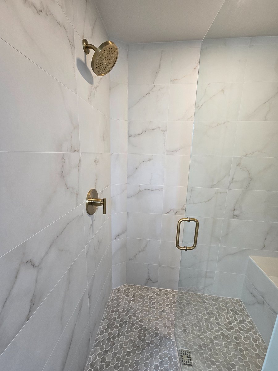 The master shower boasts stunning tile work enhanced by elegant, brushed gold fixtures, elevating its luxurious appeal to the next level.
