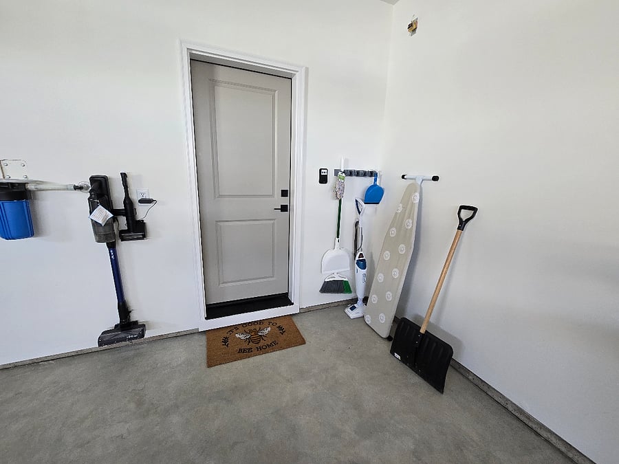 There is designated storage space just outside the door leading into the garage, where you will find a broom, steam mop, ironing board, and vacuum cleaner, all conveniently organized for easy access and storage.