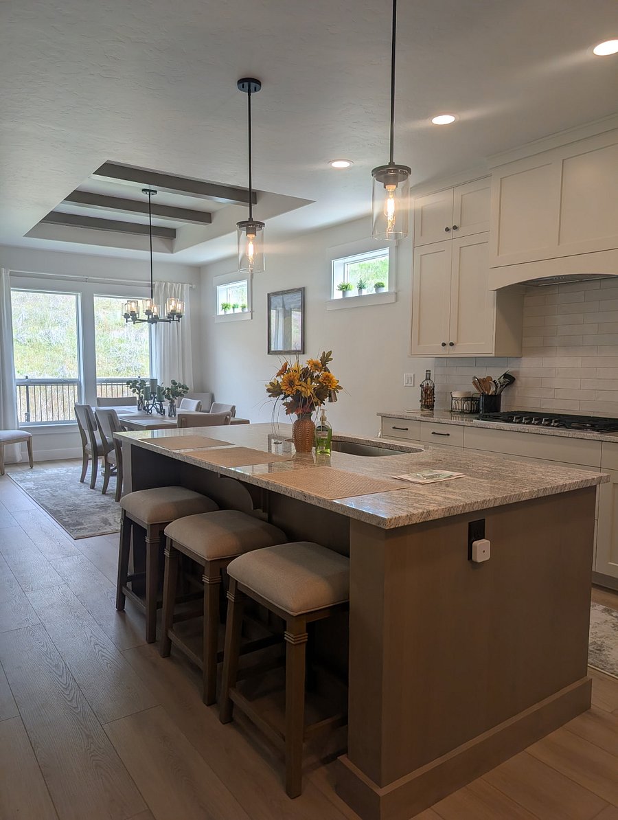As you step into the open-concept living space, you'll notice the kitchen island with comfortable breakfast bar stools, featuring a stunning granite countertop and offering a clear view of the dining area and the outdoors.