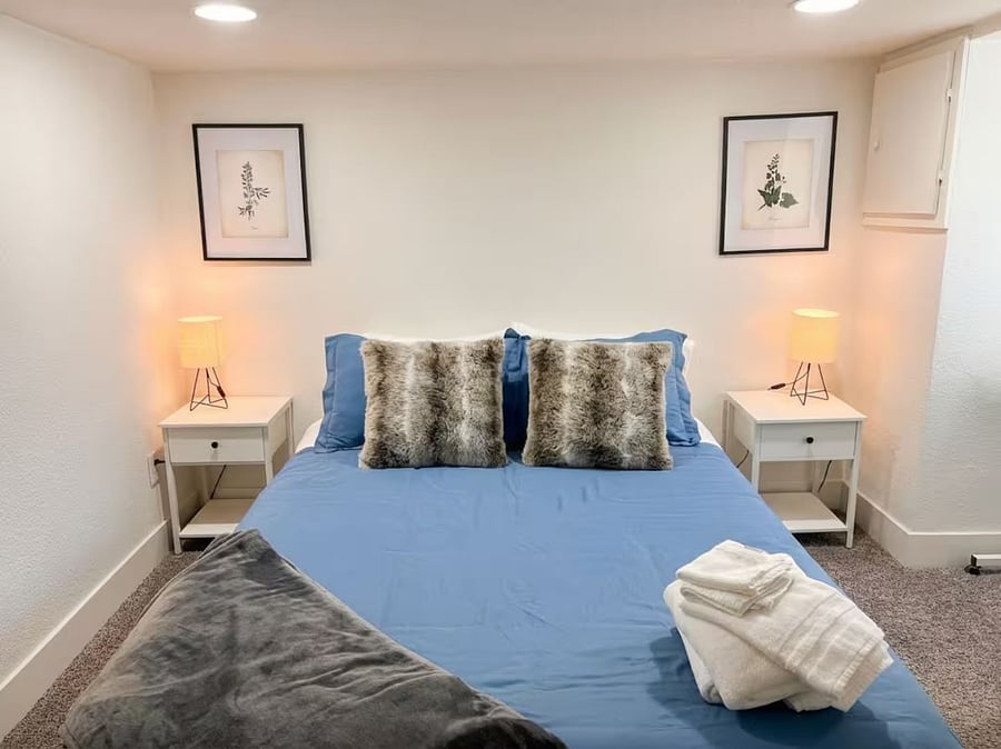 Second bedroom with a queen bed with botanical art, faux-fur pillows, and bedside lamps.