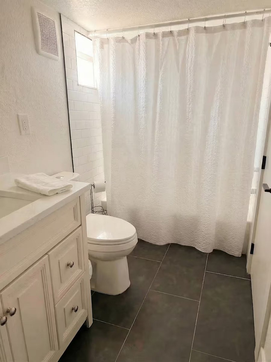 Full btahtroom with shower/tub combo, dark slate floors, and white vanity.