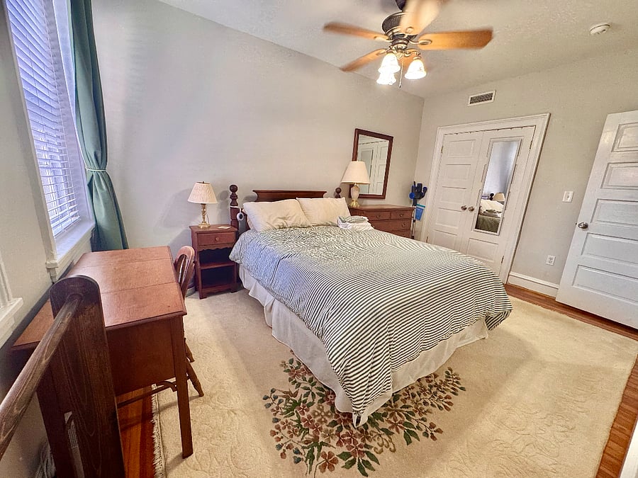bedroom with queen sized bed, dresser, desk, large closet, ceiling fan.